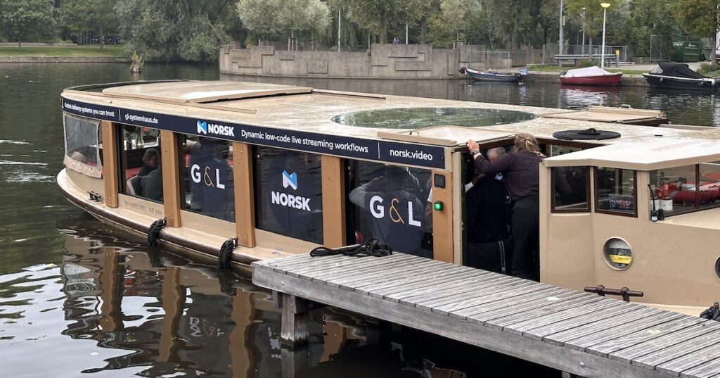 Photo of a canal cruise boat docked at the RAI in Amsterdam at IBC 2023, with the company names and logos for Norsk and G&L on the windows.