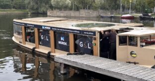 Photo of a canal cruise boat docked at the RAI in Amsterdam at IBC 2023, with the company names and logos for Norsk and G&L on the windows.